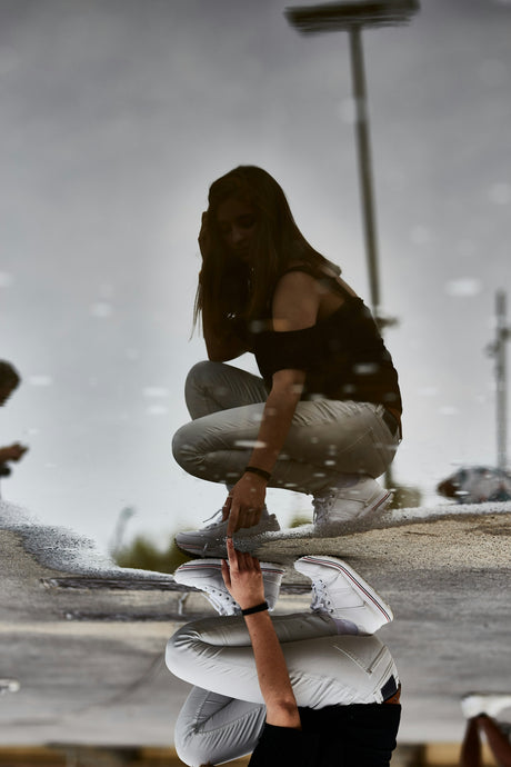 woman in black off-shoulder shirt with gray denim jeans pointing on the water with her reflection during daytime
