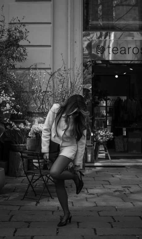 A woman adjusts her shoe outside a store.
